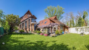 Una casa a due piani con tetto spiovente, prato curato e diverse piante e alberi.