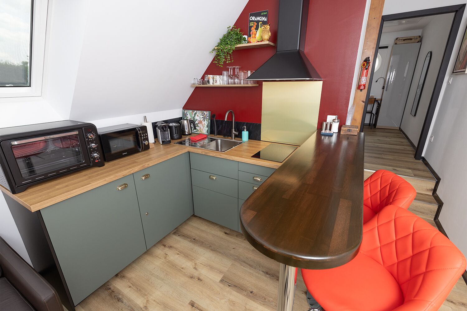Eine kleine Küche mit Mikrowelle, Toaster und Spüle. Auf der Arbeitsfläche steht ein roter Stuhl und ein Topf mit Pflanze.