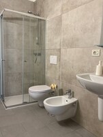 Un bagno con doccia vetrata, un water, un bidet e un lavabo.