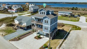 A two-story house with a balcony and a covered porch, located near a road and water body.