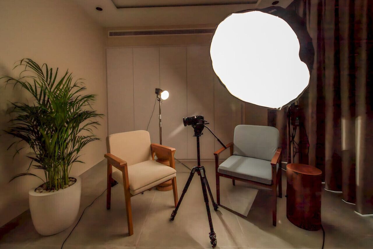 Ein Raum mit einer auf einem Stativ montierten Kamera, einer großen Softbox-Lampe und zwei Stühlen.