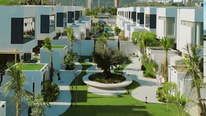 A modern hotel courtyard with white buildings, green lawns, and palm trees. - Twin room in Private villa (Dubai)