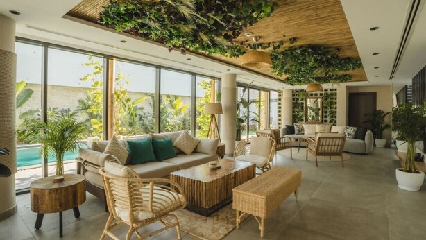A spacious living area with a high ceiling adorned with greenery, large windows offering views of the outdoors, and a variety of seating arrangements including sofas and chairs. - Twin room in Private villa (Dubai)