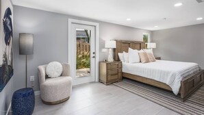 A modern bedroom with a large bed, bedside tables, a chair, and a view through a glass door to an outdoor area. - Starfish Contemporary Home (Sarasota)