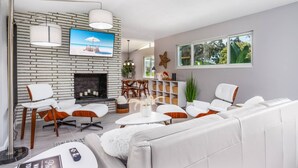 A modern living room with a brick wall, a fireplace, white furniture, and a large window. - Starfish Contemporary Home (Sarasota)