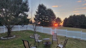 A backyard with a white picket fence, a fire pit, and outdoor seating. - Whispering Pines Manor

 (Johnstown)