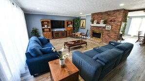 A living room with a blue sofa, a wooden coffee table, and a brick fireplace. - Whispering Pines Manor

 (Johnstown)