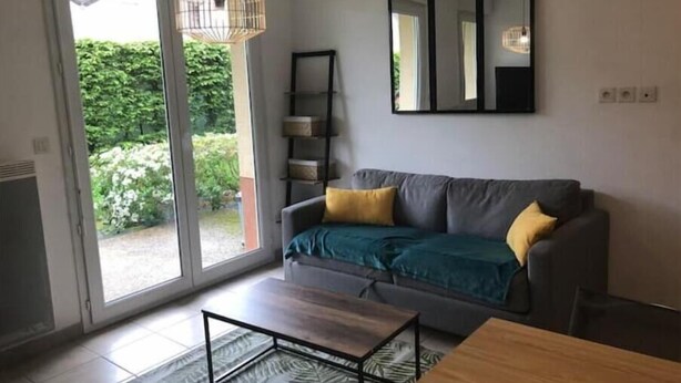 A living room with a grey sofa, yellow cushions, a wooden coffee table, and a large mirror on the wall. - Appartement en Résidence Sécurisée Circuit 2kms (Le Mans)