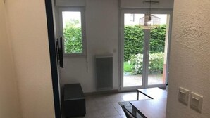A room with a tiled floor, a bench, a table, and a sliding glass door leading to a garden. - Appartement en Résidence Sécurisée Circuit 2kms (Le Mans)
