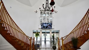 A grand staircase with wooden railings and a chandelier, leading to a glass door entrance. - Beautiful Jacuzzi Suite with Garden View/Studio (Shanty Bay)