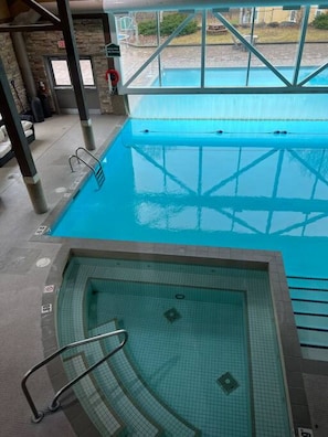 An indoor swimming pool with clear water, a diving board, and a view of the outside.