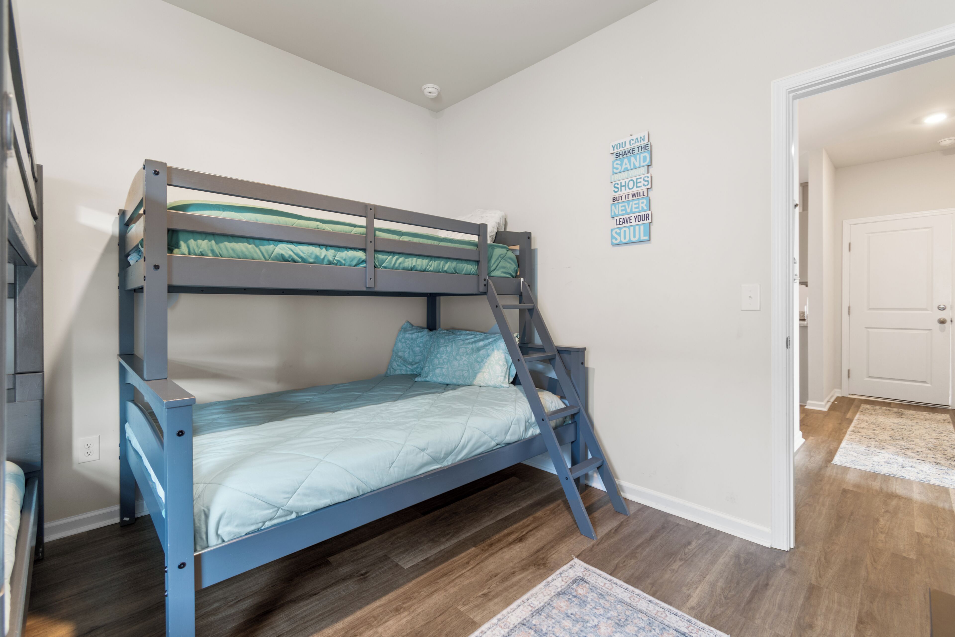 Una cama litera con escalera, una pequeña alfombra y una cita motivadora en la pared.