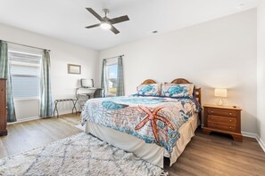 A bedroom with a bed, a desk, a chair, a nightstand, and a ceiling fan.