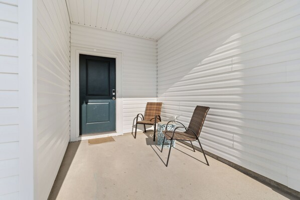 A covered porch with a door, two wicker chairs, and a small table.