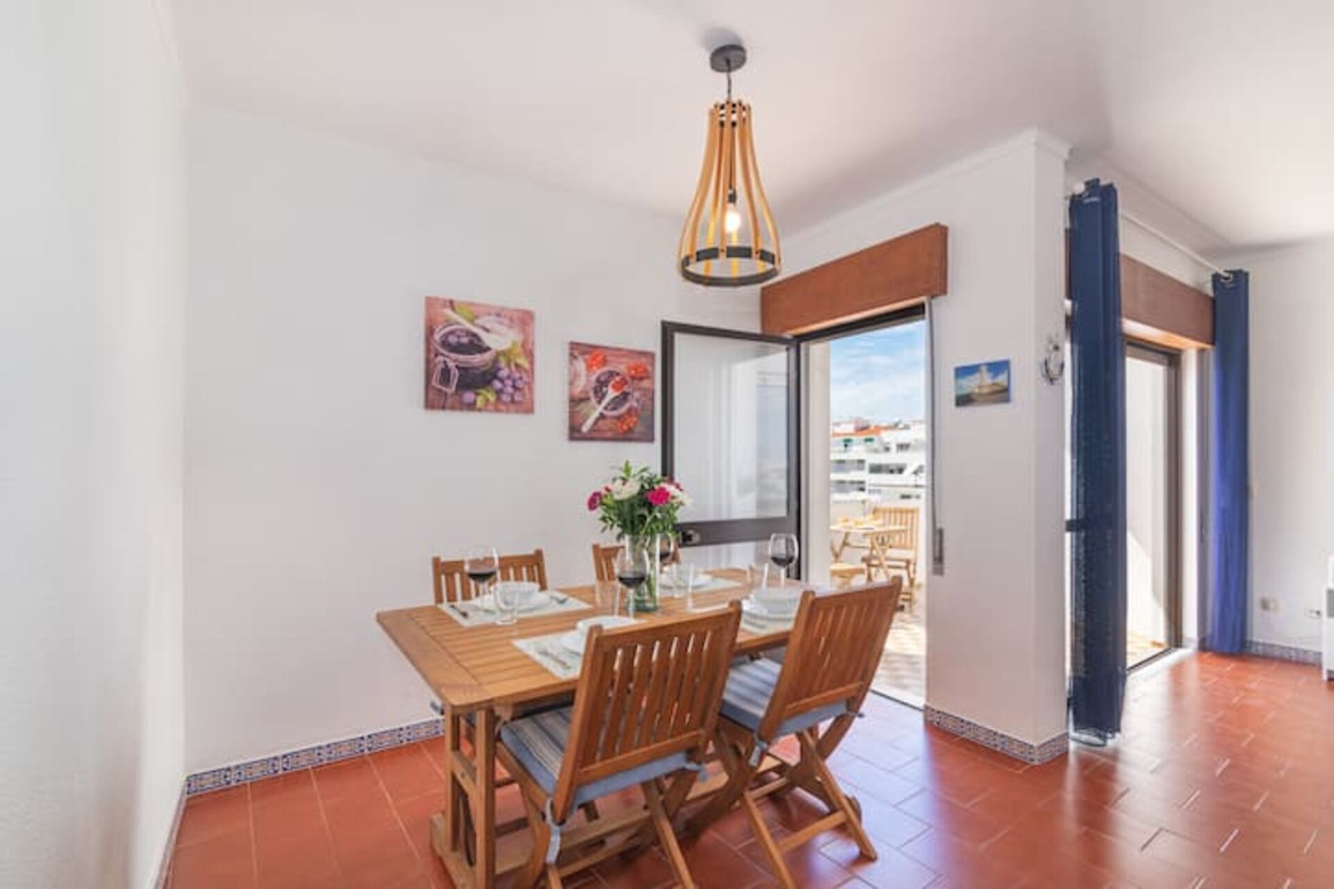 Un comedor con una mesa y sillas de madera, una lámpara colgante y obras de arte en las paredes.