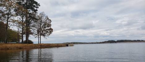 Un lago tranquilo con árboles a la izquierda y un cielo nublado.