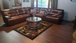 Ein braunes, ledernes Ecksofa mit einem Glastisch in der Mitte, einem gemusterten Teppich und Holzböden.