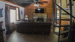Ein Wohnzimmer mit braunem Ledersofa, Kamin, Deckenventilator und Wendeltreppe.