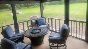 Ein überdachter Patio-Bereich mit einem runden Tisch und vier Stühlen, mit Blick auf einen Rasen mit Feuerstelle und einer Holzterrasse.