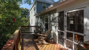 A wooden deck with a chair and a bench, a glass door, and a house in the background. - Colington Harbour OBX Cottage (Kill Devil Hills)