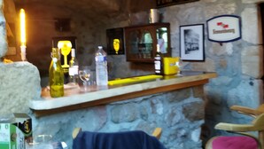 A rustic bar area with stone walls, a wooden bar counter, and a clock. There are bottles, glasses, and a chair visible. - mas Cévenol en Ardèche Animaux Acceptés (rosieres)