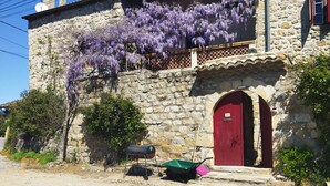 A stone building with a red door, a small porch, and purple flowering vines. - mas Cévenol en Ardèche Animaux Acceptés (rosieres)
