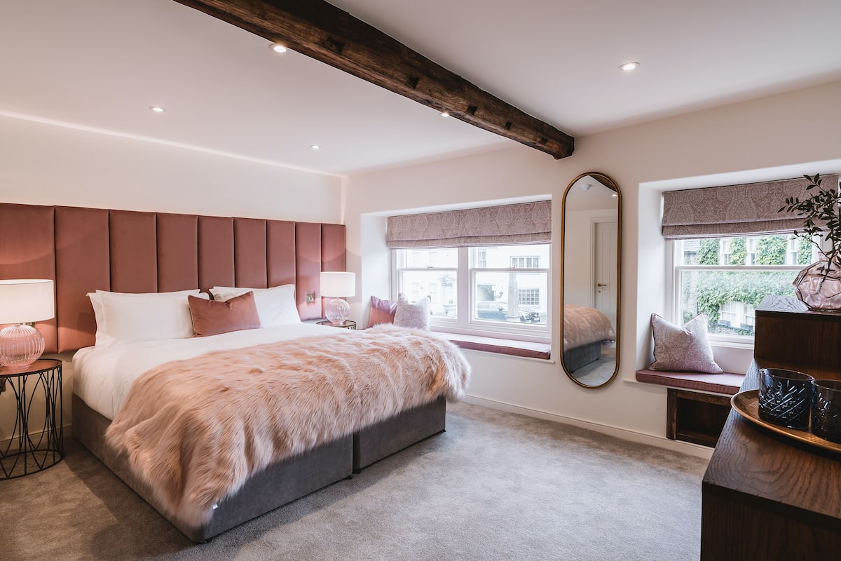 Une chambre avec un grand lit, une fenêtre donnant sur un beau paysage, un miroir et un banc placé près de la fenêtre.