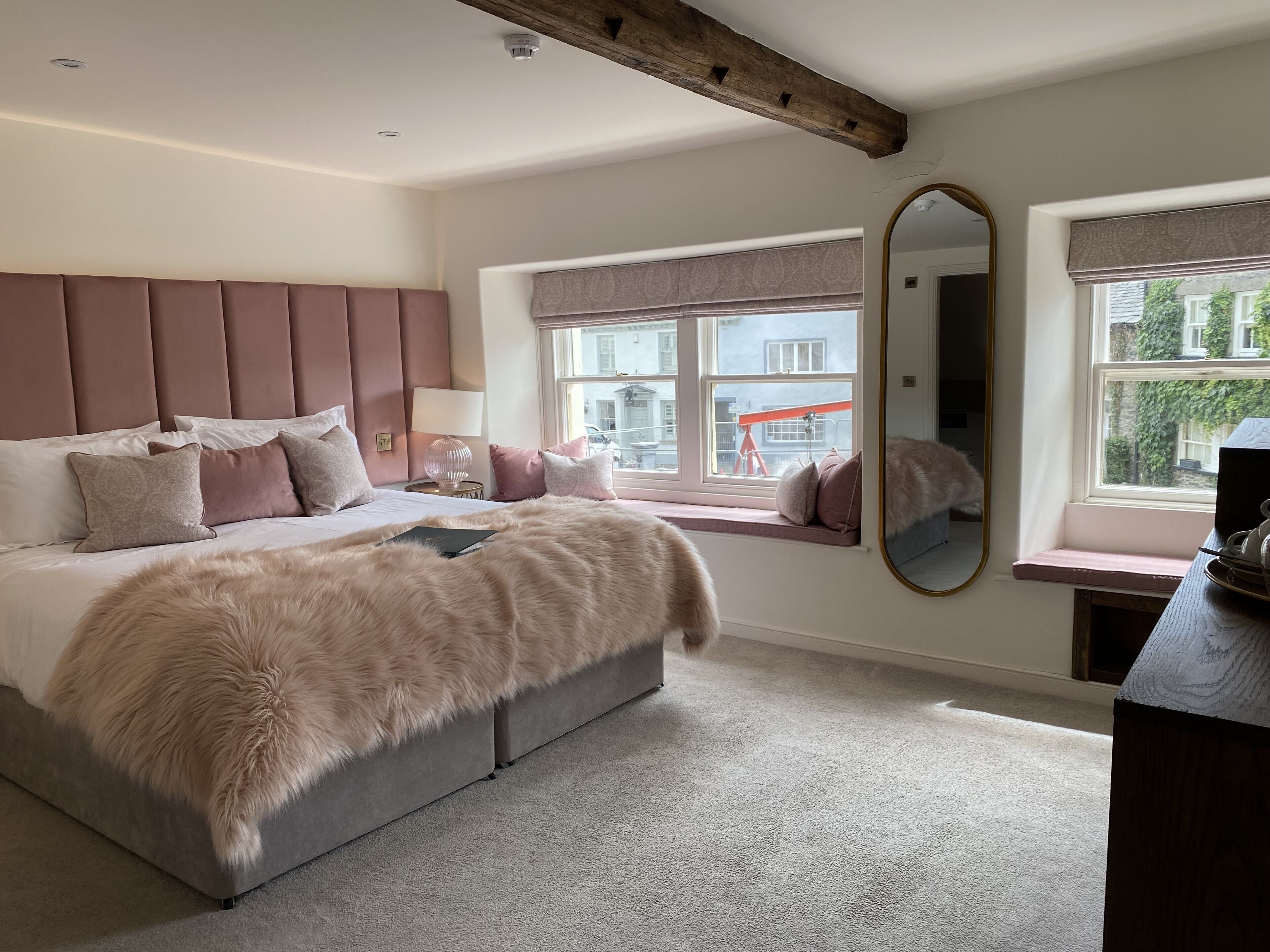 A bedroom with a large bed, a window with a view, a mirror, and a bedside table.