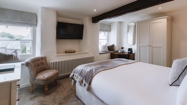 A bedroom with a large bed, a chair, a TV mounted on the wall, and a window with a view. - Coffee & Stays at Cartmel Square (Grange-over-Sands)