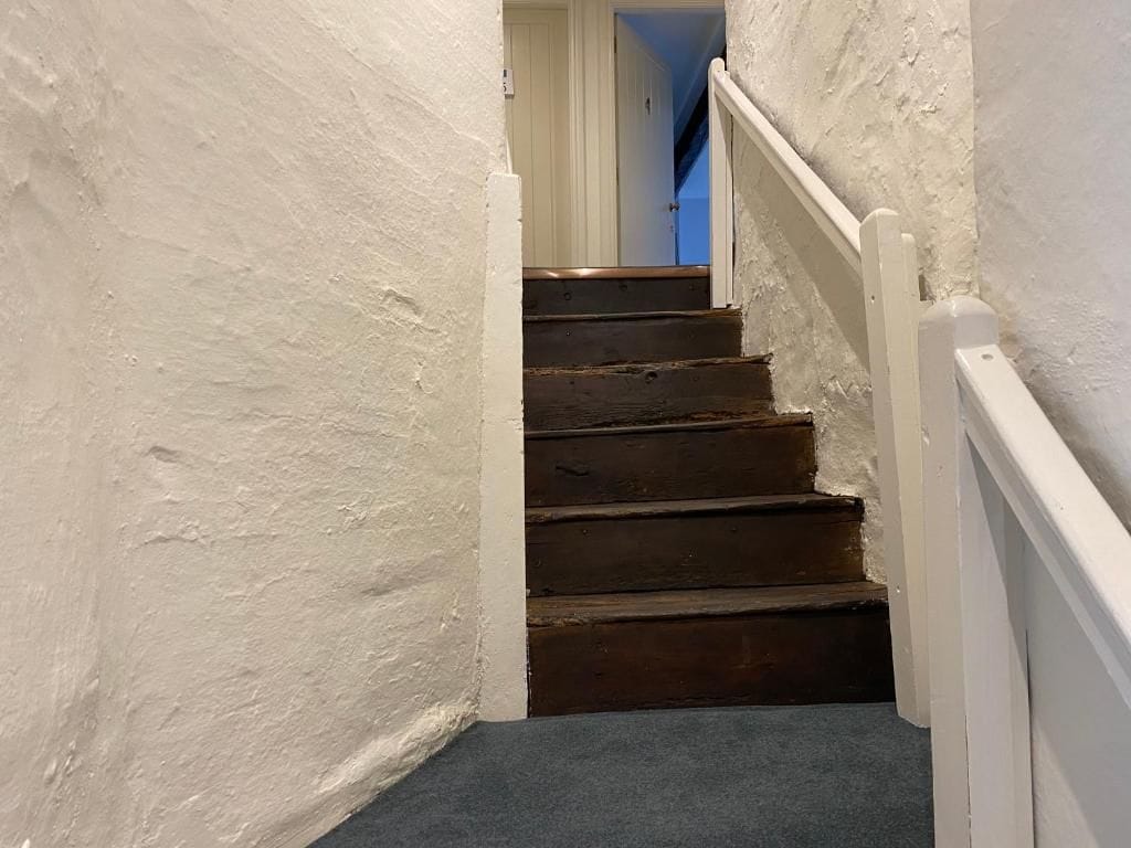 Una escalera de madera con barandillas blancas que lleva a una puerta.