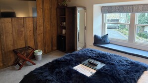 A room with a wooden wall, a large mirror, a wardrobe, a window with a view, and a fluffy rug. - Coffee & Stays at Cartmel Square (Grange-over-Sands)