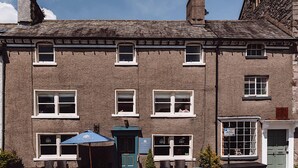 A two-story building with multiple windows, a door, and outdoor seating with umbrellas. - Coffee & Stays at Cartmel Square (Grange-over-Sands)