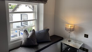 A room with a window, a bench, and a table with a lamp. - Coffee & Stays at Cartmel Square (Grange-over-Sands)