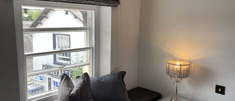 A room with a window, a bench, and a table with a lamp.