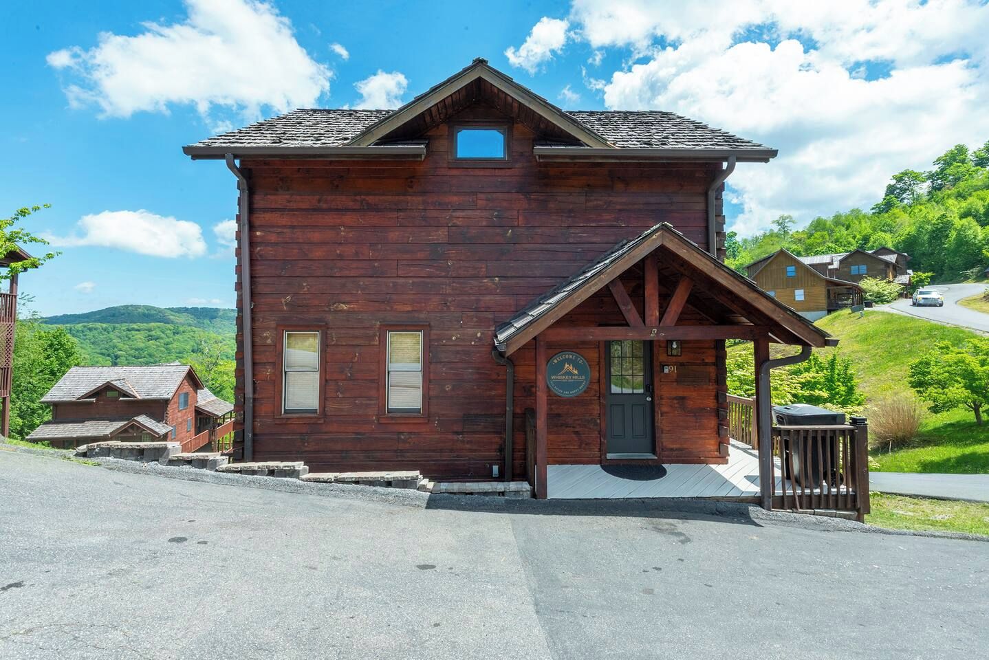 Un chalet en bois doté d’un porche, d’une pancarte d’accueil et offrant une vue sur le paysage environnant.