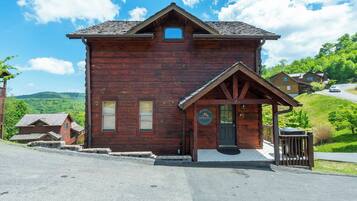 A wooden lodge with a porch, a welcome sign, and a view of the surrounding landscape.