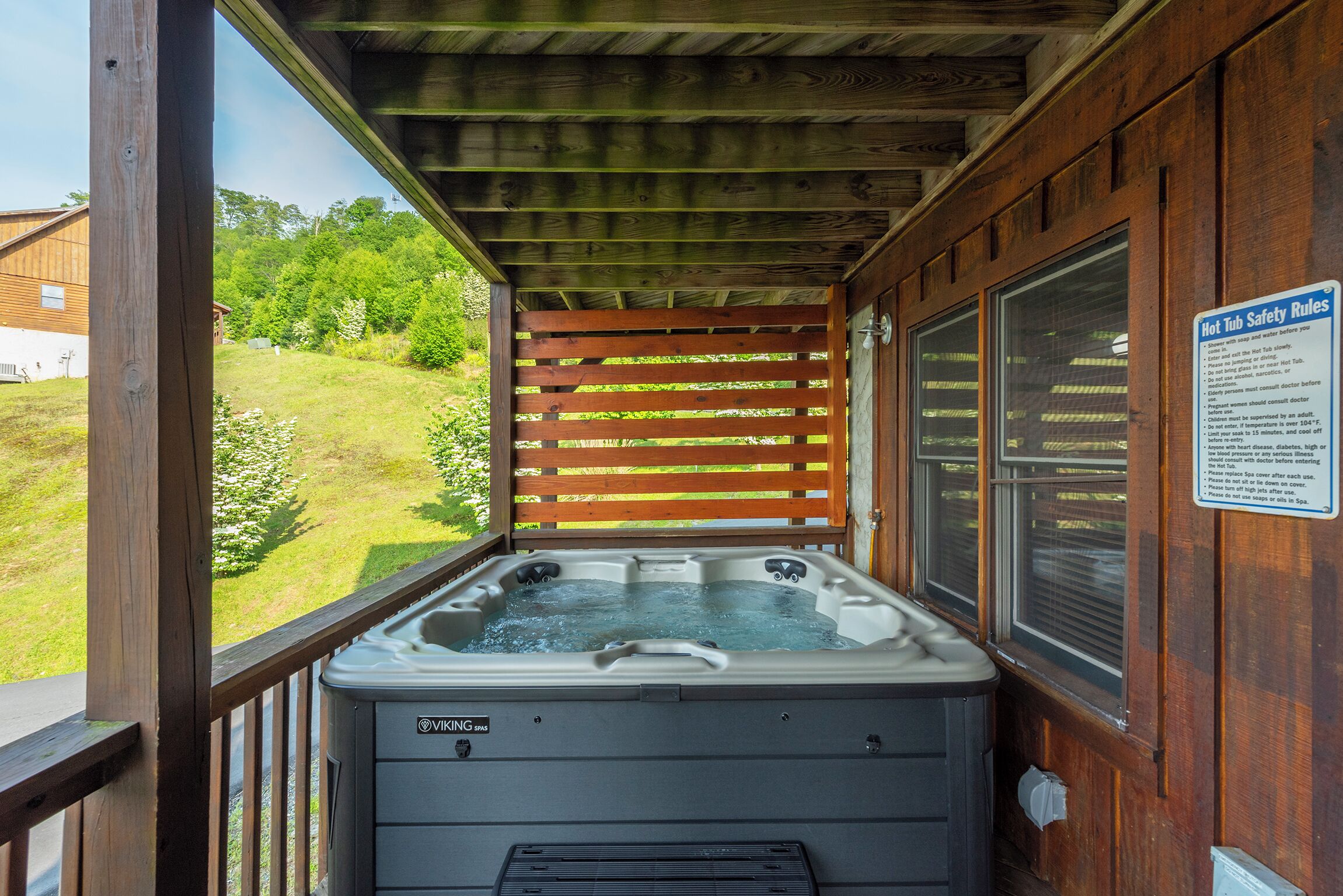 Un jacuzzi en una cabaña de madera con un letrero de seguridad, una terraza de madera y vista a un espacio cubierto de césped.