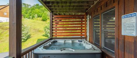 Un jacuzzi en una cabaña de madera con un letrero de seguridad, una terraza de madera y vista a un espacio cubierto de césped.