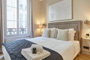 A hotel room with a bed, a nightstand, a lamp, and a window with a view of buildings. - Sublim new flat center of Paris Opéra Madeleine (Paris)