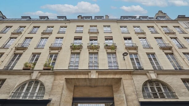 A multi-story building with a symmetrical facade, large windows, and balconies with plants.