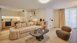 A modern living room with a sofa, a coffee table, and a chair. There is a kitchen area with cabinets and a countertop.