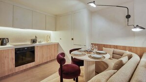 A modern kitchen with a dining area, featuring a built-in oven, a round dining table with a light fixture above, and a sofa with a wooden accent wall.