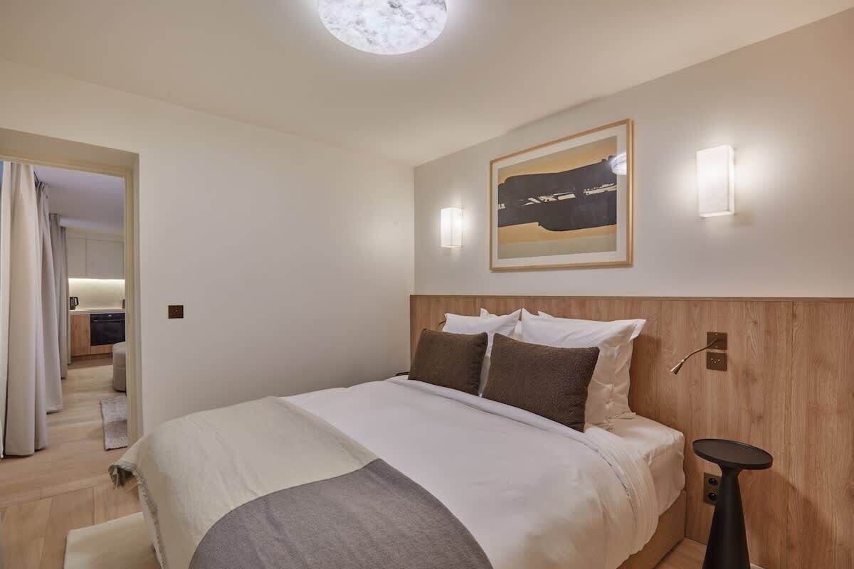 A hotel room with a large bed, a wooden headboard, a framed artwork above the bed, and a small side table.