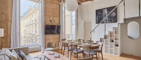 A modern living room with a wooden ceiling, large windows, a dining area, and a staircase.