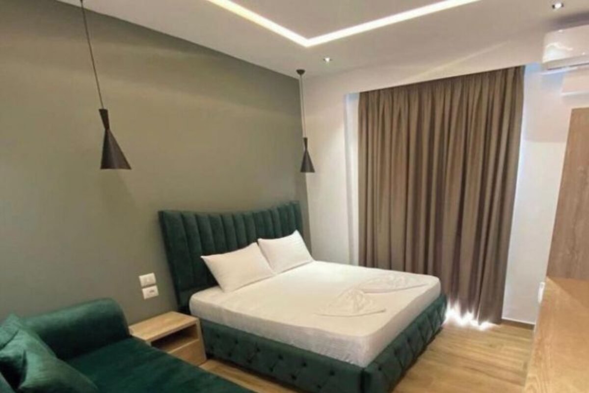 A modern bedroom with a large bed, a green sofa, wooden flooring, and a window with curtains.