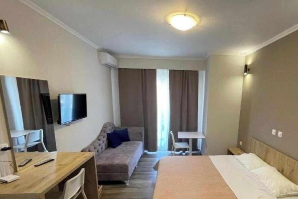 A hotel room with a bed, a desk, a sofa, a TV, and a window with curtains.