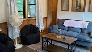 Ein gemütliches Wohnzimmer mit Holzbalkendecke, Deckenventilator, einer Couch, zwei Sitzsäcken, einem Couchtisch und einem Fenster mit Vorhängen.