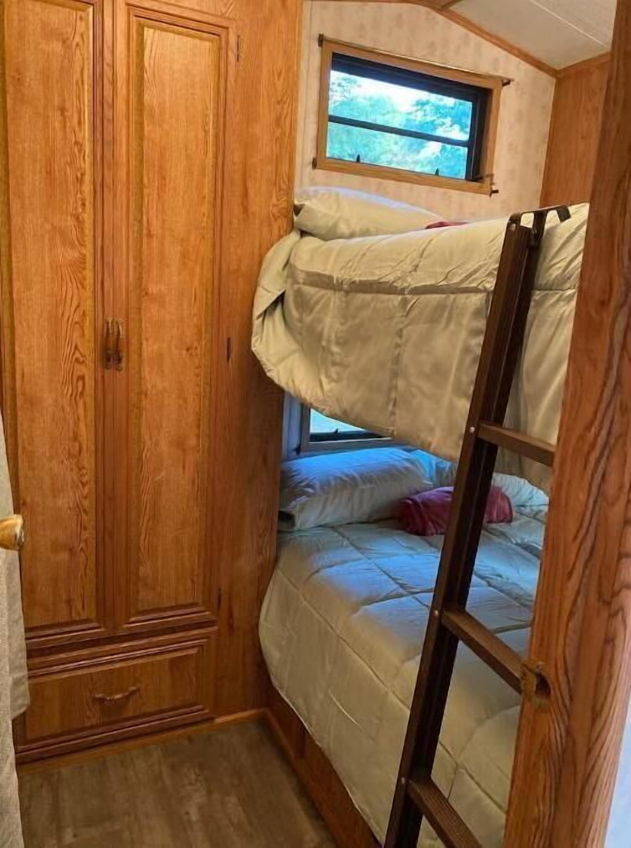 A bunk bed room with a wooden wardrobe and a window.