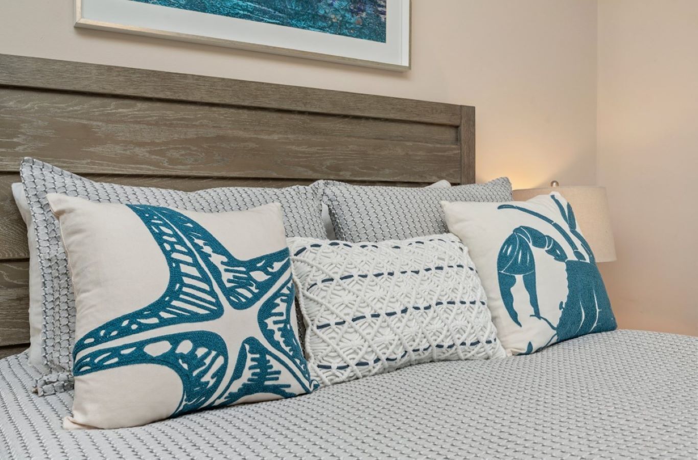 Un lit recouvert d’une couverture blanche à motifs, doté d’une tête de lit en bois et agrémenté de trois coussins décoratifs aux motifs géométriques.