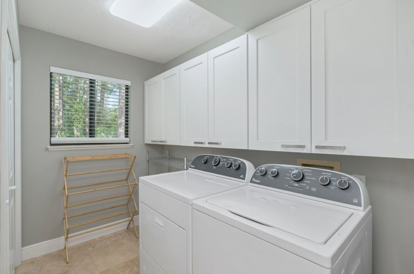 A laundry room with a front-loading washer and dryer, a drying rack, and white cabinets.